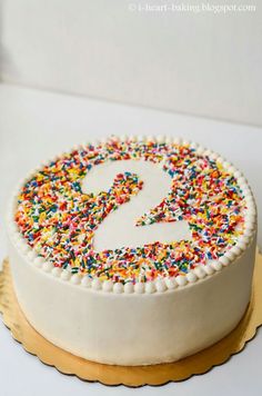 a white cake with sprinkles and a number 2 on the top is sitting on a gold plate