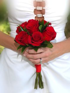 a bride holding a bouquet of red roses in her hands and wearing a wedding ring