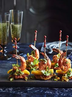 several appetizers are arranged on a black plate with wine glasses in the background