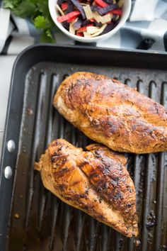 two pieces of chicken on top of a grill next to a bowl of veggies