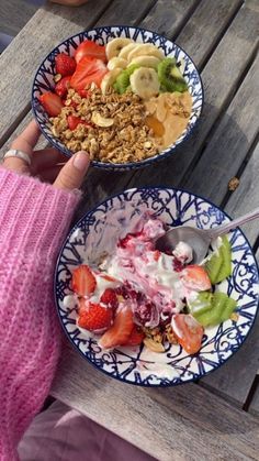 two bowls of fruit and yogurt sit on a picnic table next to a woman's hand