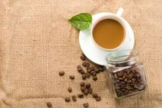 a cup of coffee sitting on top of a table next to some beans and leaves