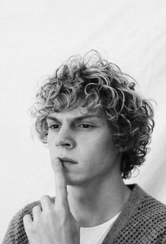 a young man with curly hair holding his finger to his nose