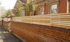 a brick wall with wooden slats on the top and bottom, next to a sidewalk