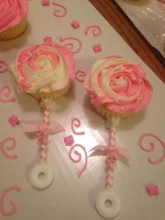 three cupcakes with pink frosting and white icing on top of a table