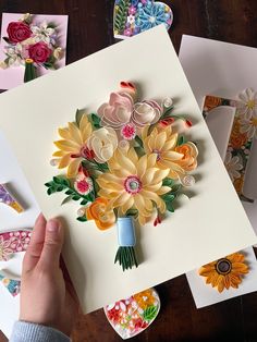 a person is holding some paper flowers on a table next to cards and magnets