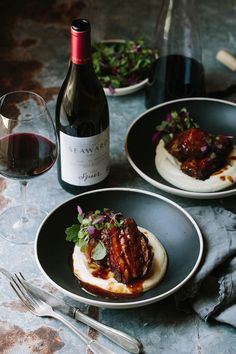 two plates with food on them next to a bottle of wine