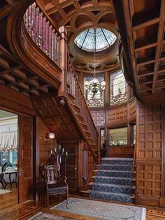 an ornate wooden staircase in the center of a room with wood paneling and glass windows