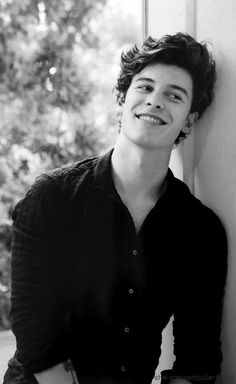 a young man leaning against a wall and smiling