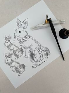 a drawing of two rabbits on paper next to a pair of scissors and some ink