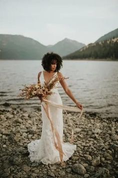 a woman in a white dress standing on rocks near the water holding a bouquet with flowers