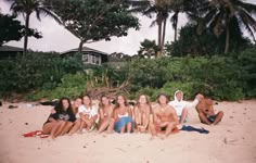 a group of young people sitting on top of a sandy beach next to palm trees