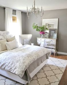 a white bed sitting in a bedroom next to a chandelier above a mirror