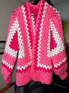 a pink and white crocheted sweater hanging on a rack