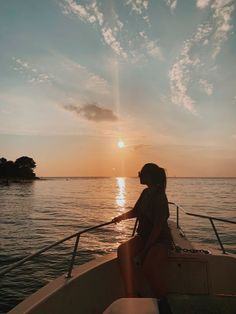 a woman is sitting on the bow of a boat at sunset, looking out to sea