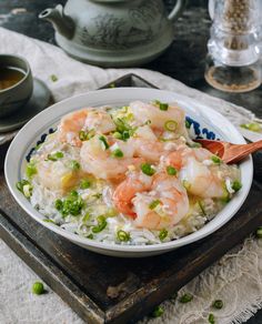 a bowl filled with rice and shrimp on top of a wooden tray next to a tea pot