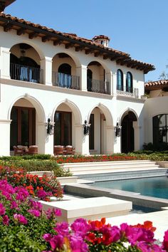 a large house with flowers in front of it and a pool surrounded by greenery