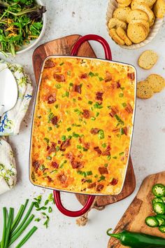 a casserole dish on a cutting board surrounded by vegetables and crackers