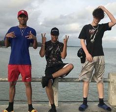 three young men sitting next to each other on a pier near the water with their hands in the air