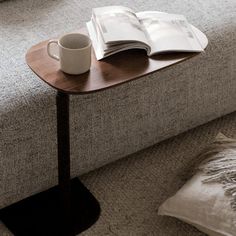 a coffee cup on a table next to an open book and a pillow in a living room