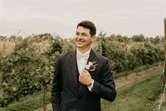 a man in a tuxedo smiles as he stands next to a vineyard