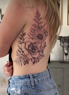 the back of a woman's stomach with flowers and leaves tattooed on her chest