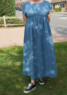 a woman standing in the grass wearing a blue dress