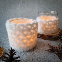 two white candles sitting on top of a table next to pine cones and orange slices