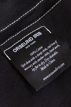 a label on the back of a black shirt with white stitching and an orselund iris logo