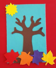 a paper cutout of a tree surrounded by fall leaves on a red background with the sun and stars above it