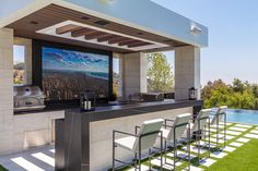 an outdoor bar with four chairs and a television on the wall next to it in front of a swimming pool