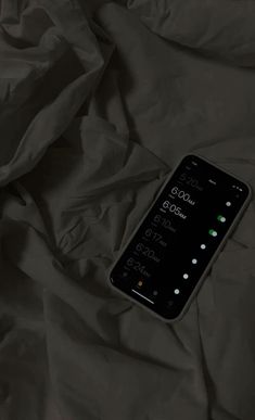 a cell phone laying on top of a bed covered in black sheets and blankets,