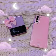 two cell phones laying next to each other on top of a white blanket with pink bows