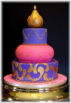 a three tiered cake is decorated with purple and pink icing, gold accents and a princess crown on top