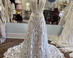 a dress on display in front of a mirror with other dresses and gowns behind it