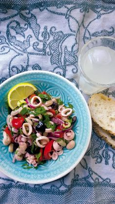 a blue plate topped with pasta salad next to a glass of water and a slice of bread