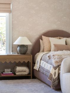 a bedroom with a bed, nightstand and lamp on the side table in front of it