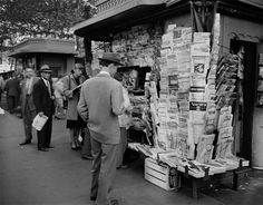 an old black and white photo of people looking at newspapers on a street side stand