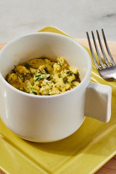 a white bowl filled with food on top of a yellow plate next to a fork