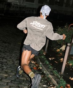 a man is running down the street at night wearing a hat and sweatpants with his feet in the air