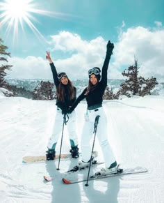 two women standing on skis in the snow with their arms up and hands raised