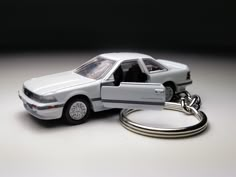 a car keychain is sitting next to a white toy car with the door open