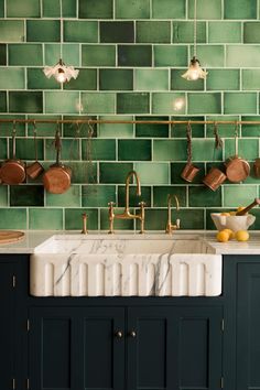 a kitchen with green tiles on the wall and white counter tops, gold faucets