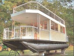 a house boat is sitting on the water in front of some trees and a tractor