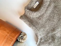 a brown leather purse sitting on top of a white table next to a sweater and hat