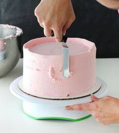 someone is cutting into a pink cake with a knife