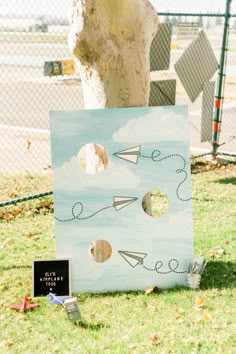 a cardboard board with paper airplanes on it in the grass next to a tree trunk