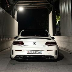 the back end of a white car parked in a parking lot at night with its lights on