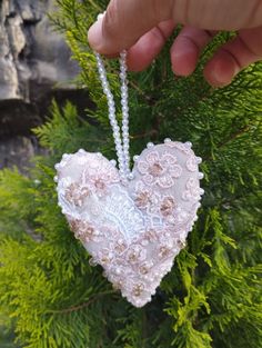 a hand holding a heart shaped ornament on a tree branch with beads hanging from it