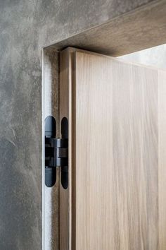 an open wooden door with black handles on a gray wall and concrete walls in the background